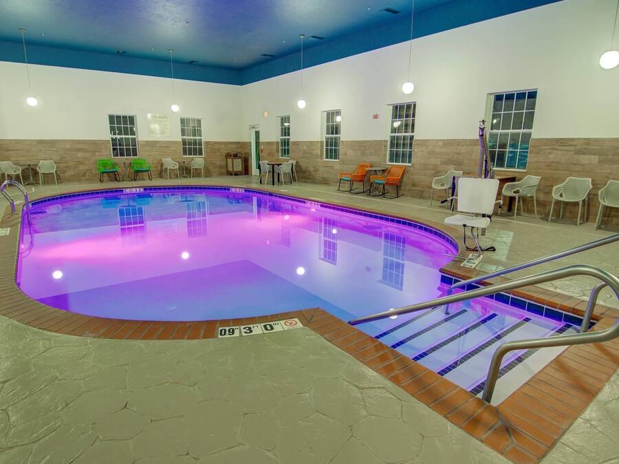 An indoor swimming pool with a blue and purple illuminated edge, surrounded by chairs and a tiled floor.