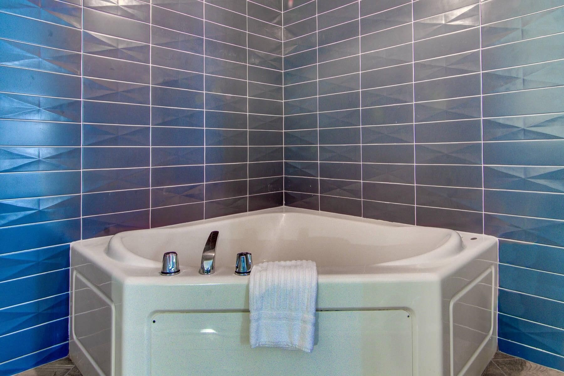 Een badkamer aan de hoek met een wit bad, een handdoek aan de zijkant en blauwe betegelde wanden.