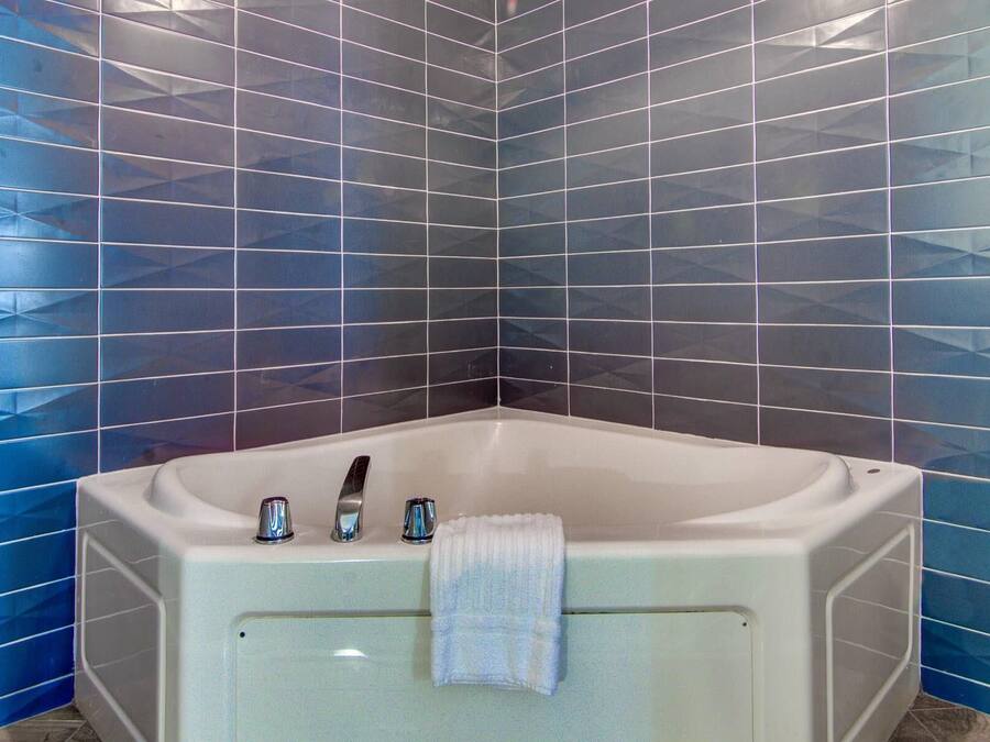Een badkamer aan de hoek met een wit bad, een handdoek aan de zijkant en blauwe betegelde wanden.