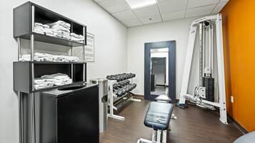 A gym with a bench, dumbbells, and Nautilus equipment.