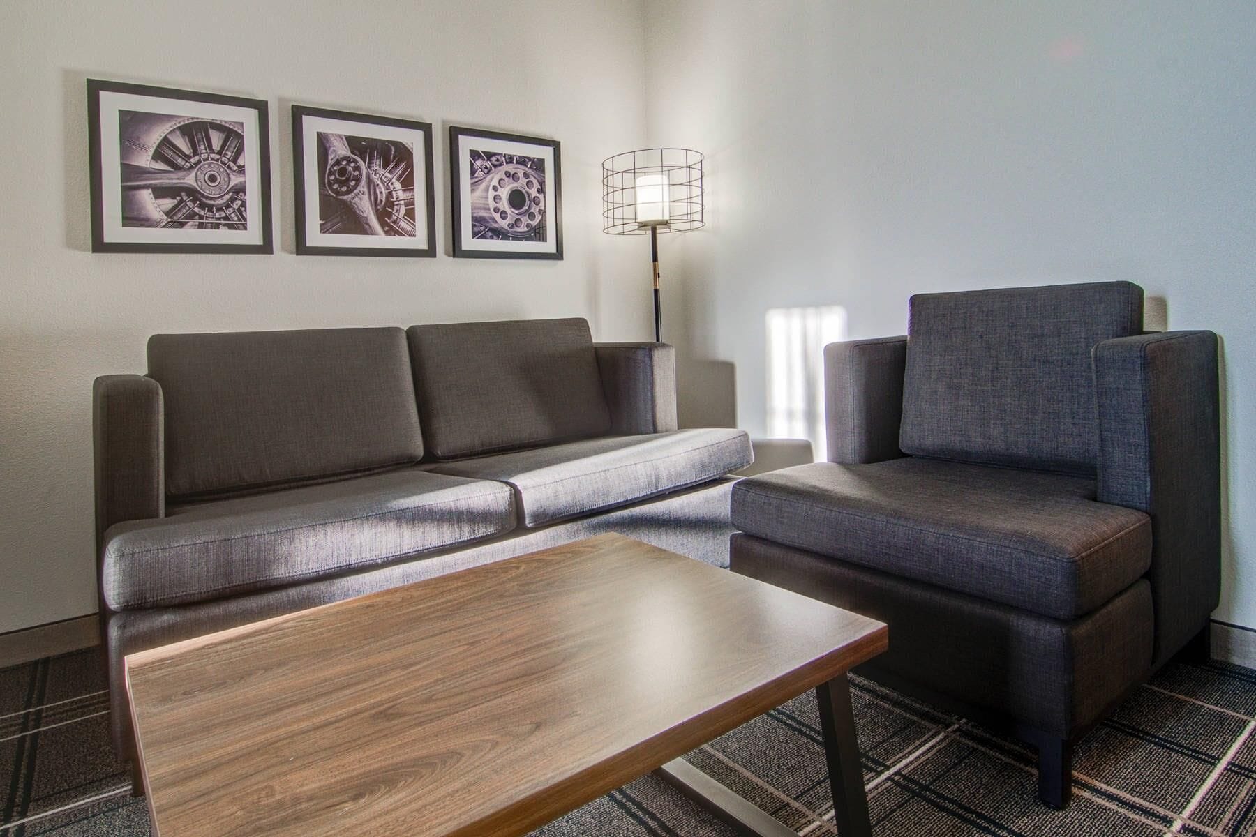 A modern living room with a sofa, armchair, and a wooden coffee table. There are three framed artworks on the wall.