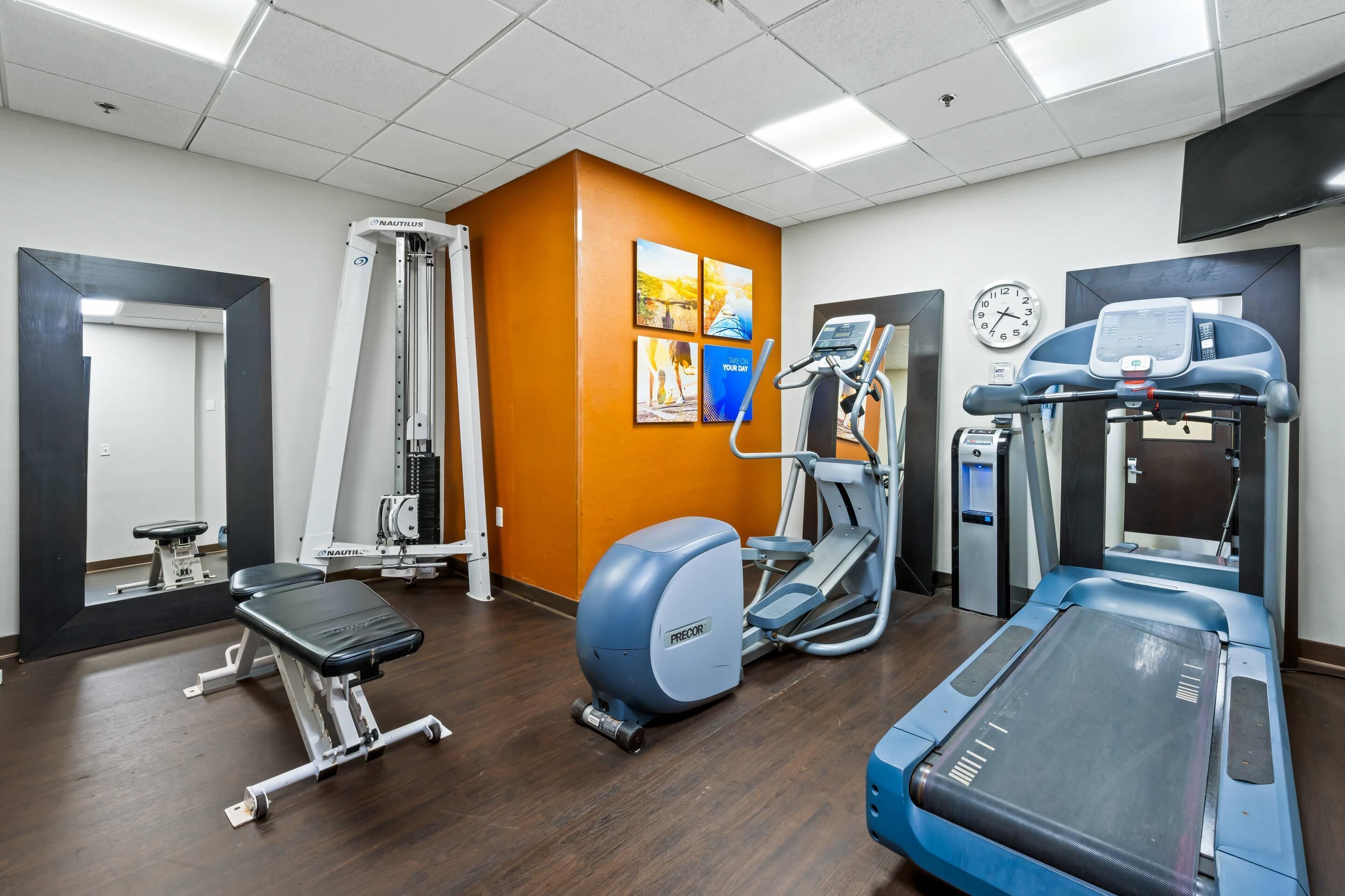 Un gimnasio con equipo Nautilus y Precor, una cinta de correr y un reloj de pared.