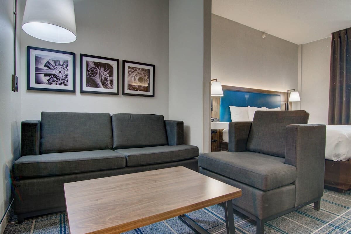Een hotelkamer met een bank, fauteuil en een klein tafeltje. Drie ingelijste foto’s hangen aan de muur.