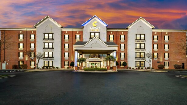 Een Comfort Suites hotel met een centrale ingang, bakstenen gevel en een opvallend logo in de vorm van een halve maan.