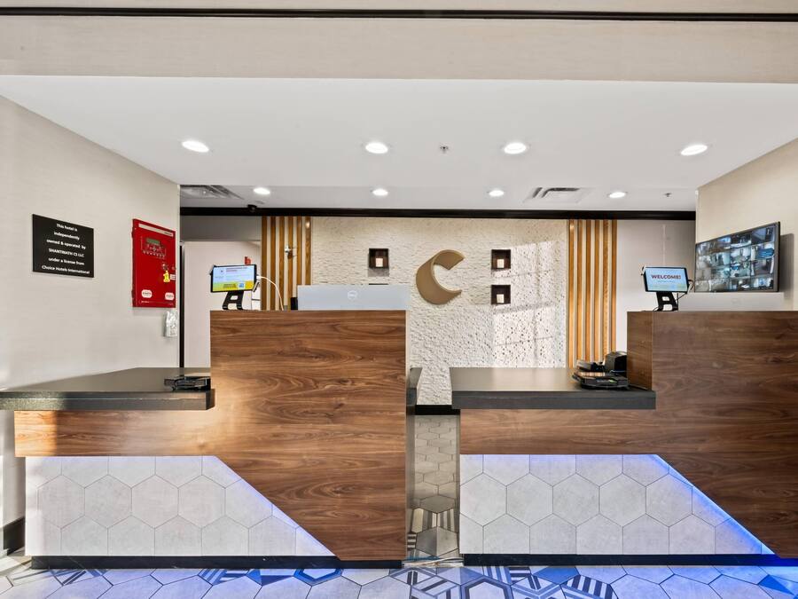 A reception area with wooden reception desks, a digital check-in kiosk, a fire alarm, and a welcome sign.