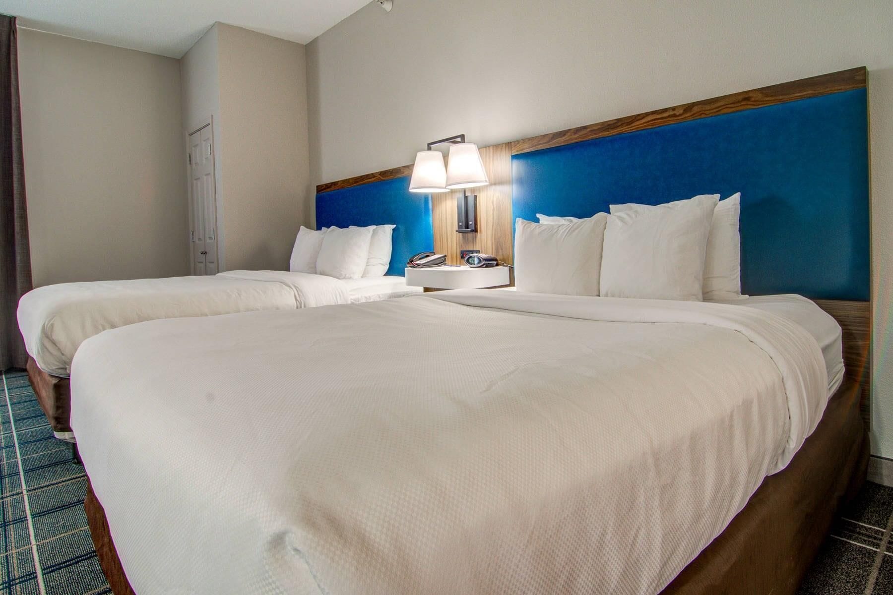 A hotel room with two beds, a bedside table with a lamp, and a phone.