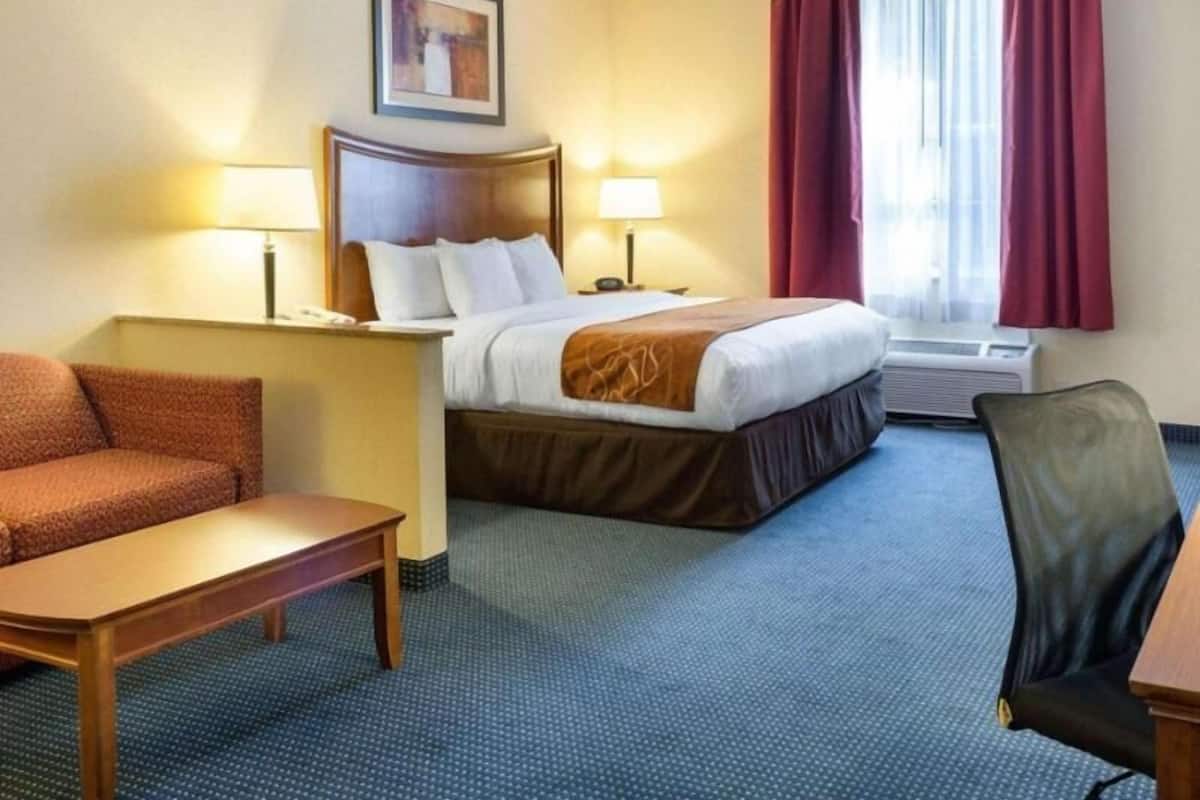 Een hotelkamer met een bed, twee nachtkastjes, een bureau, een stoel, een bank en een raam met gordijnen.