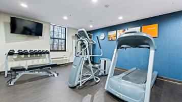 Une salle de sport équipée de matériel d’exercice, d’un téléviseur et d’une affiche motivante.