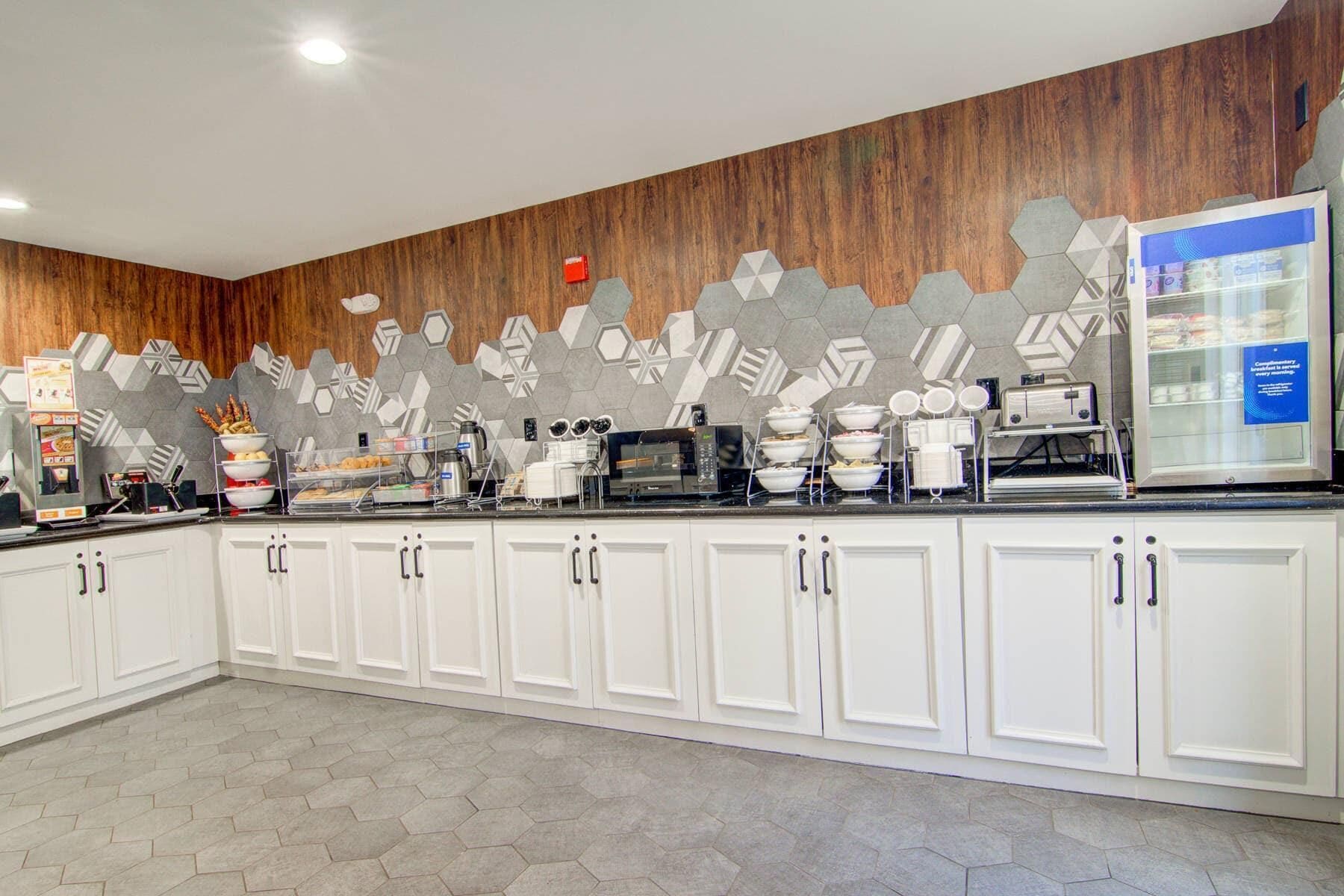 A breakfast bar with a microwave, toaster, and coffee machine, white cabinets, and a hexagonal tile floor.