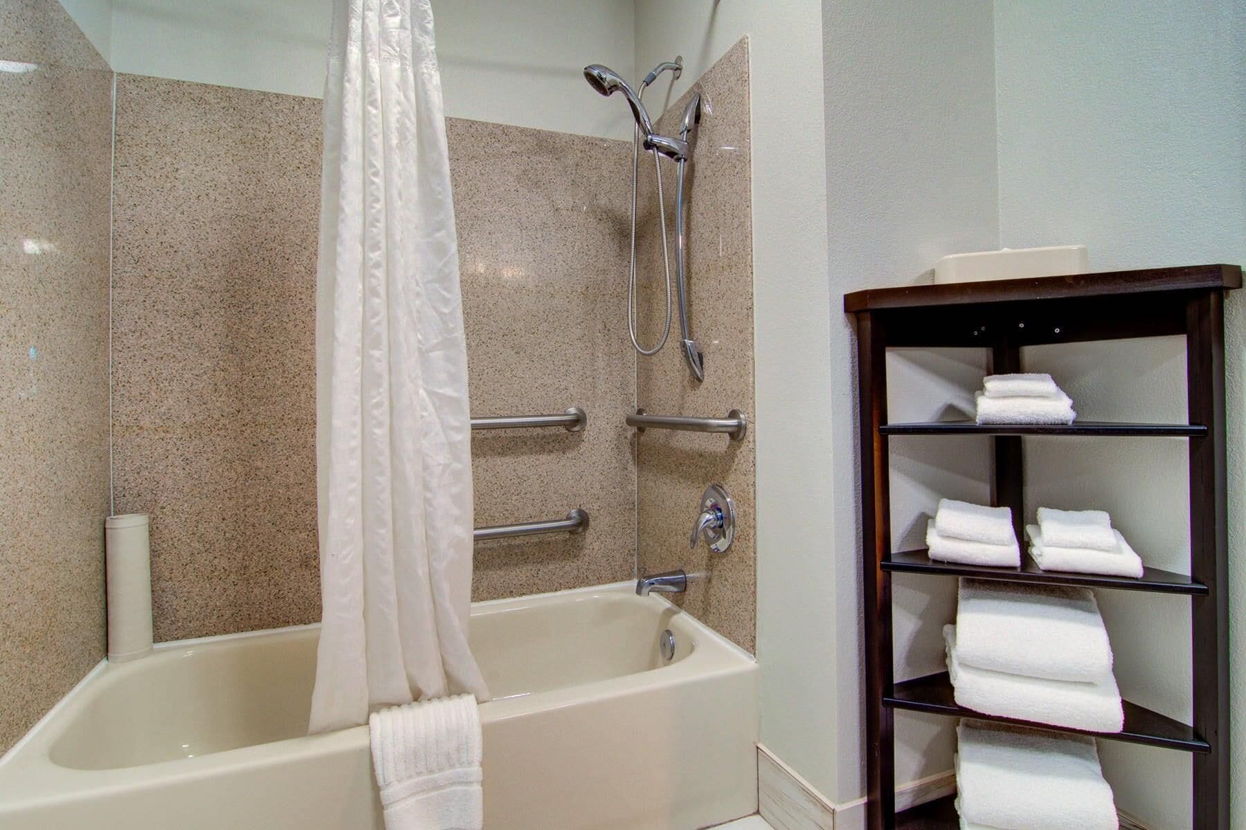 A bathroom with a bathtub, shower, and a shelf with towels.