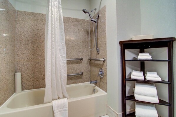A bathroom with a bathtub, shower, and a shelf with towels.