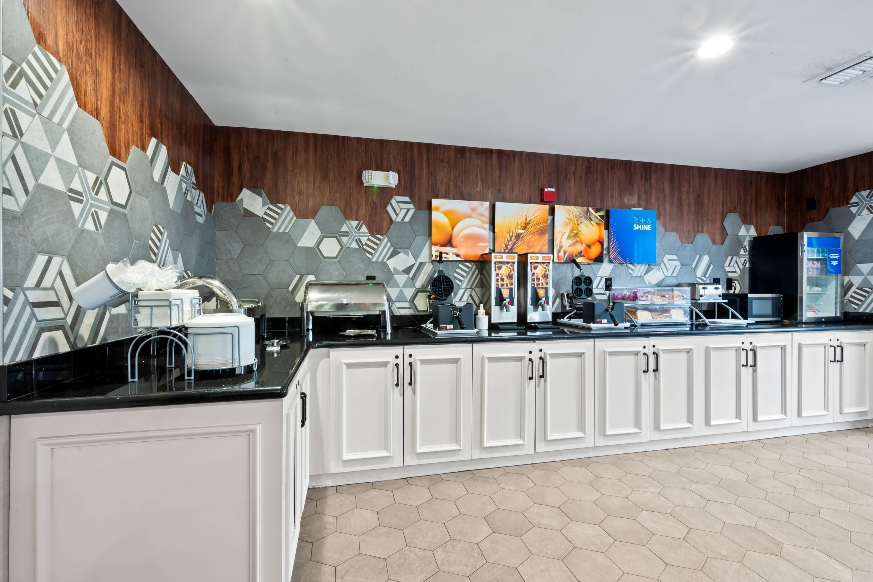 A modern kitchen with white cabinets, a black countertop, and hexagonal patterned tiles.
