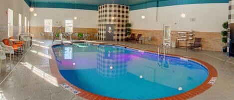 Una piscina interior con pared a cuadros, zona de estar y ventilador de techo.