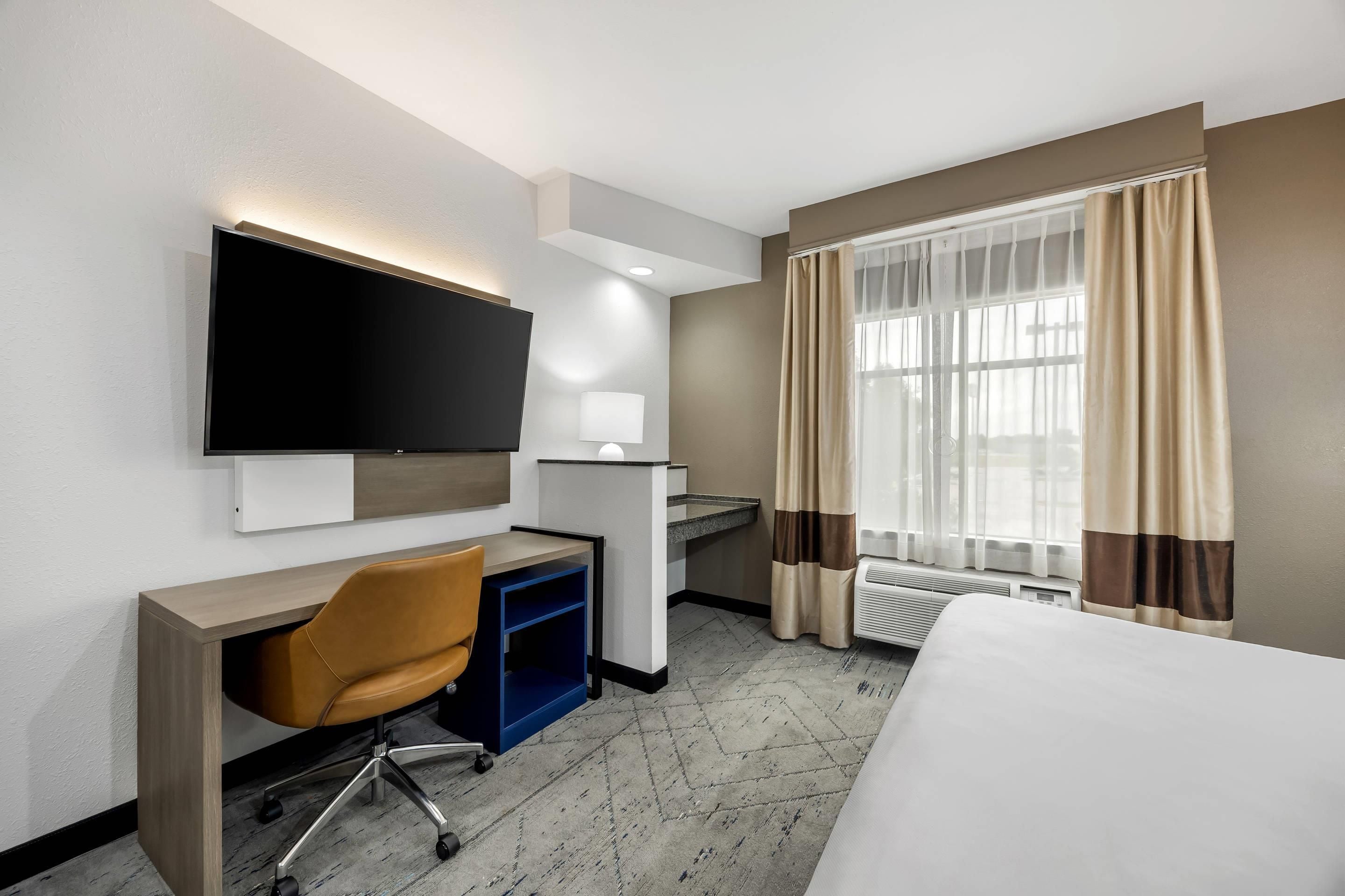 A hotel room with a bed, a desk, a chair, a television, and a window with curtains.