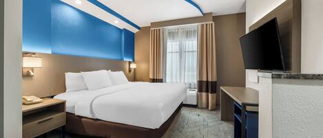 Une chambre d’hôtel comprenant un lit, des tables de chevet, un bureau, un téléviseur à écran plat et une fenêtre avec des rideaux.