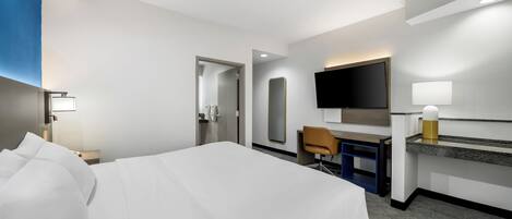 A hotel room with a bed, desk, chair, TV, and a mirror.