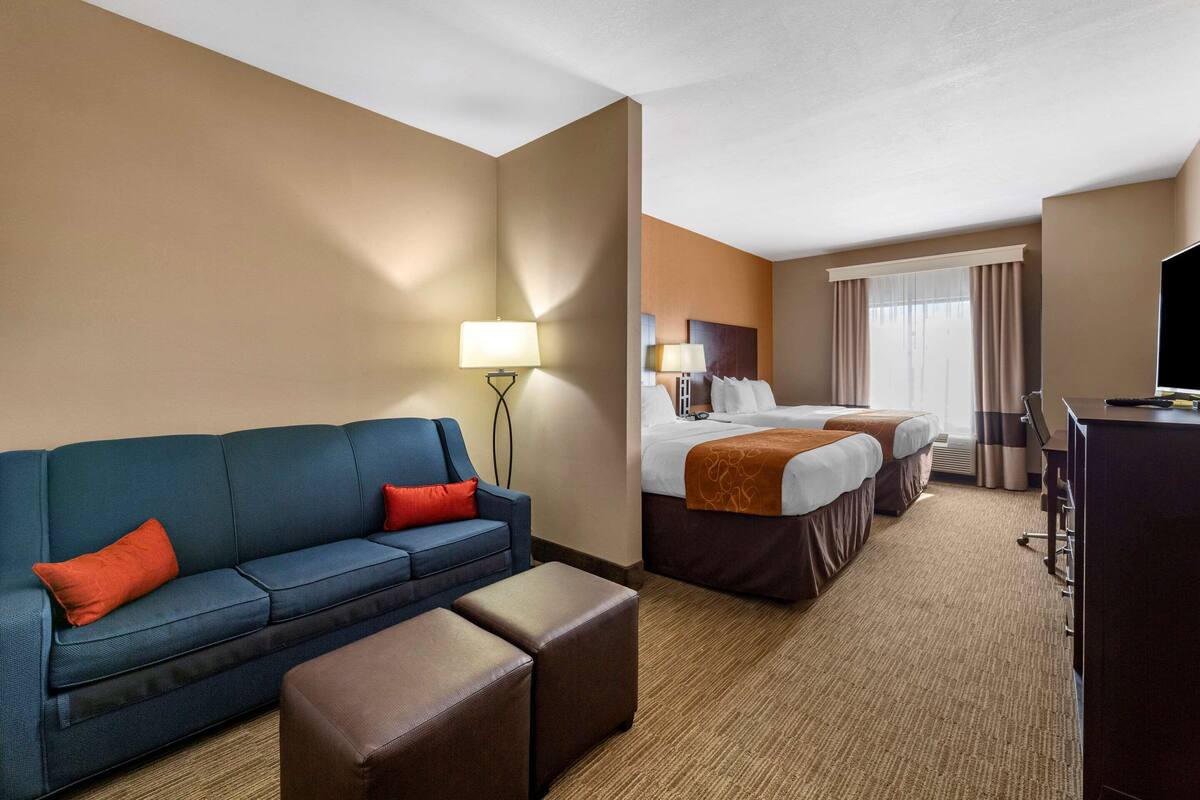 Una habitación de hotel con un sofá azul, dos camas, un escritorio y un televisor.