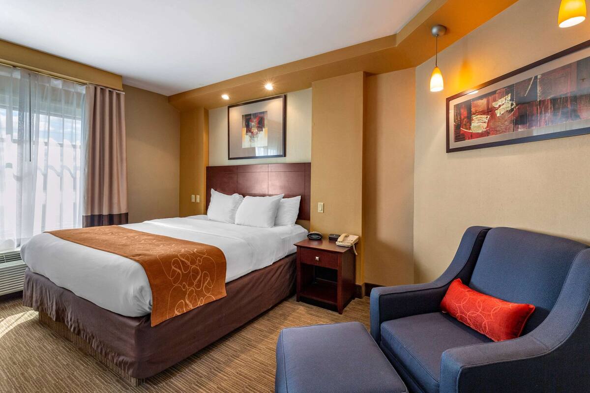 Una habitación de hotel con una cama grande, una mesita de noche con un teléfono, una silla y un cuadro en la pared.