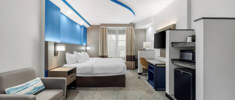A hotel room with a bed, a desk, a chair, a sofa, a television, and a refrigerator.
