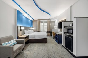Habitación de hotel con cama, escritorio, sillón, sofá, televisor y refrigerador.