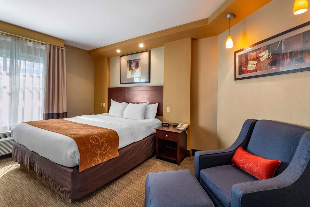 Een hotelkamer met een bed, nachtkastje, stoel en kunstwerk aan de muur.