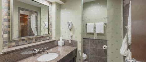 A bathroom with a granite countertop, two sinks, a mirror, a hairdryer, and a shower area.