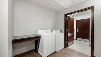 Un lavadero con dos lavadoras blancas, un escritorio de madera y una puerta que da a otra habitación.