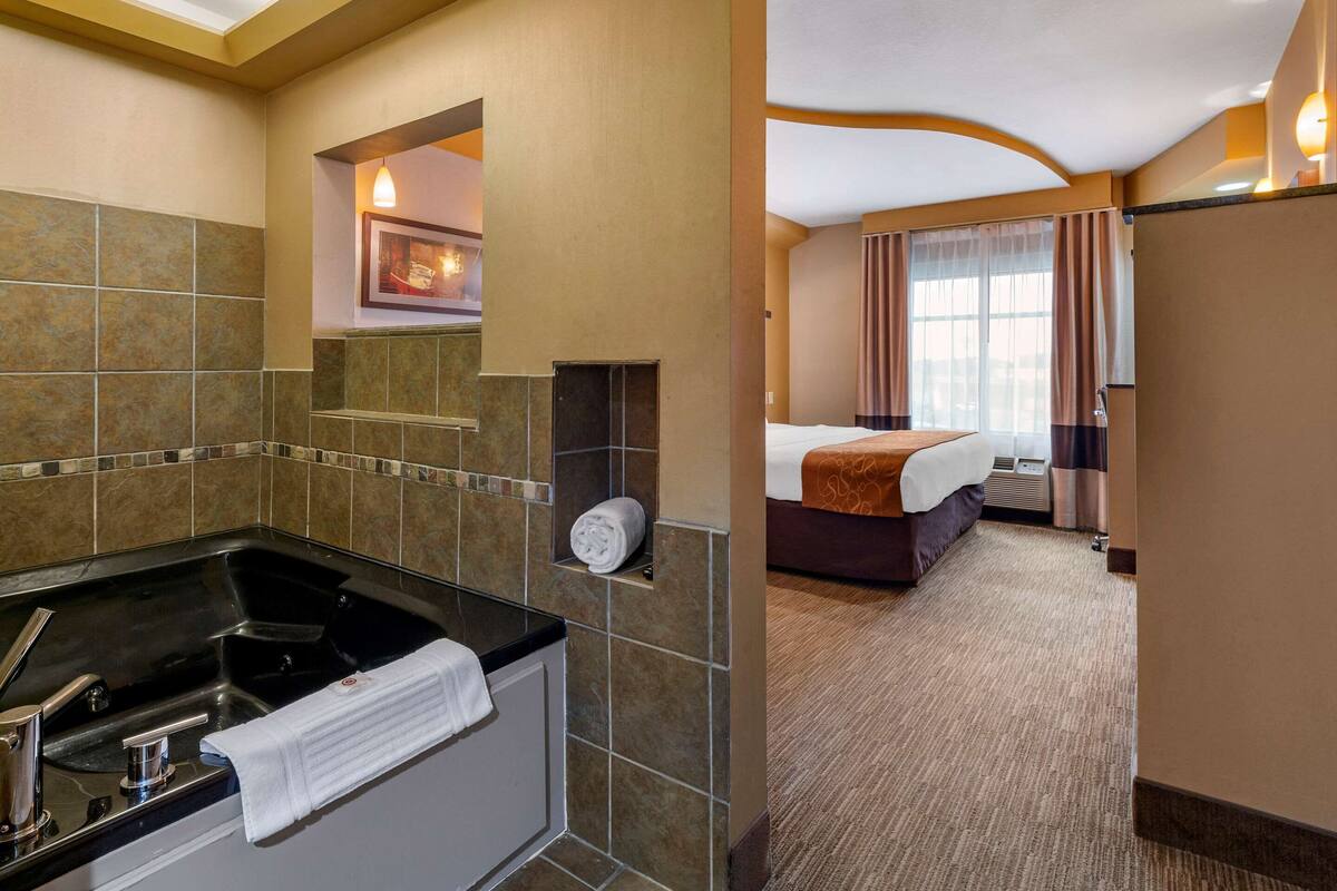 Habitación de hotel con bañera, cama, ventana con cortinas e imagen colgada en la pared.