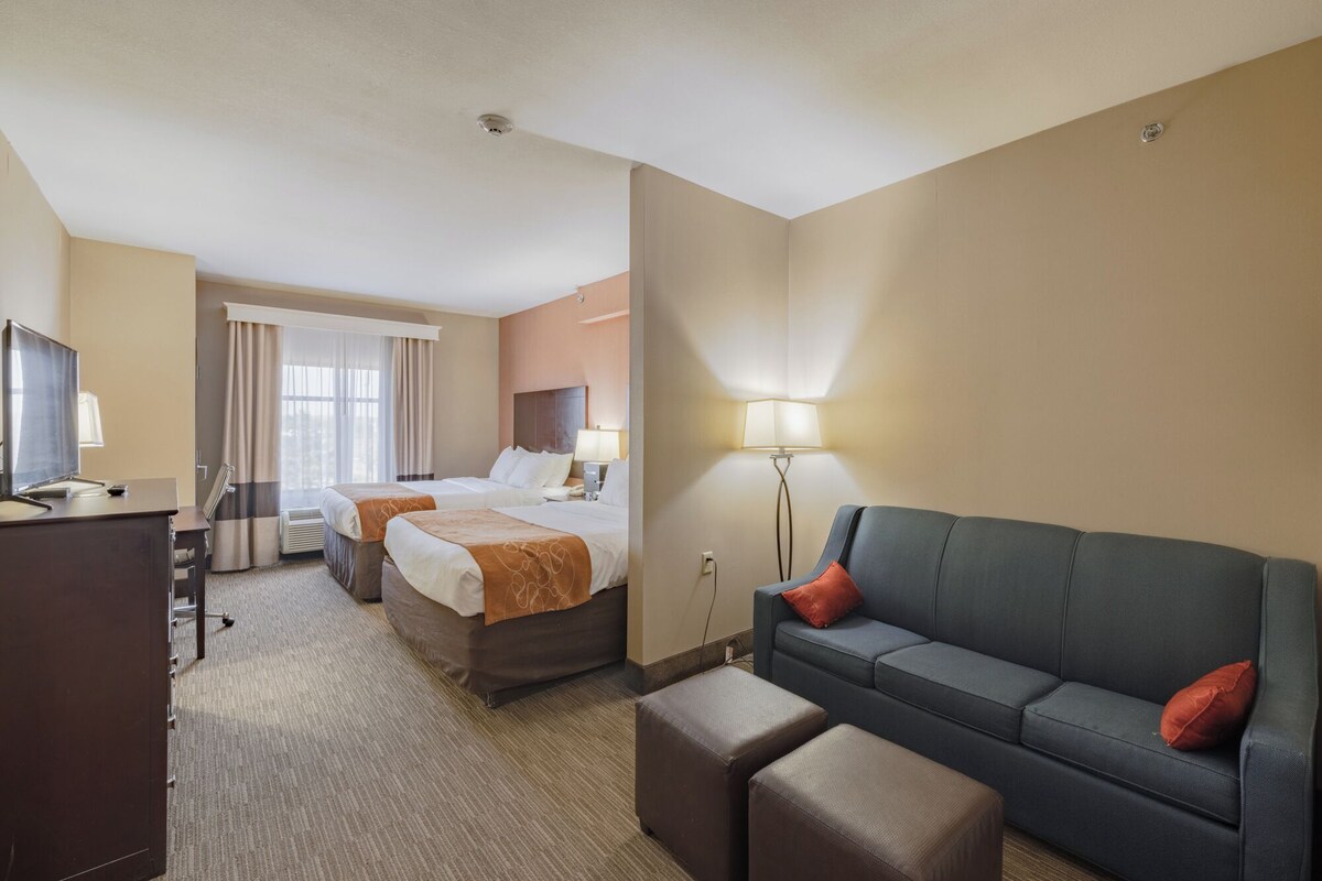 Ein Hotelzimmer mit zwei Betten, einem Schreibtisch, einem Sofa und einer Lampe.