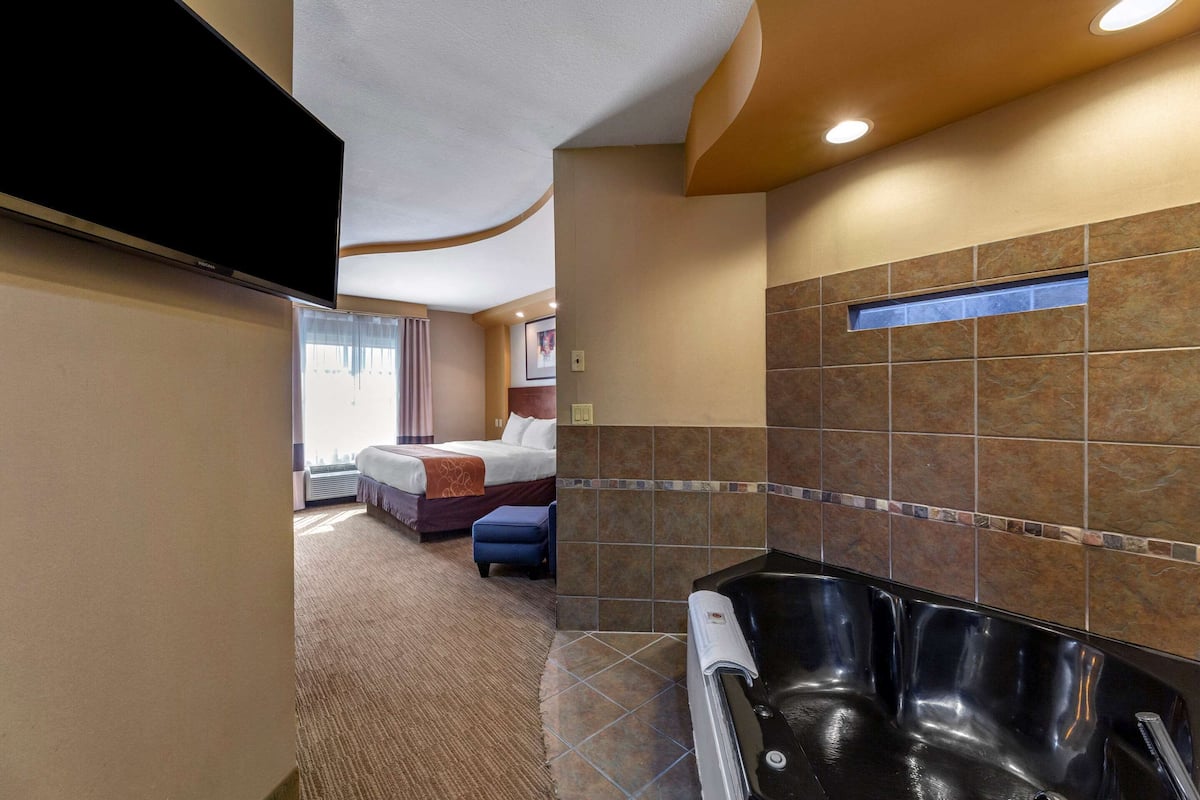 Habitación de hotel con una cama grande, baño privado con bañera y televisión de pantalla plana montada en la pared.
