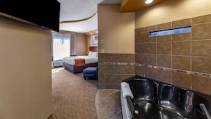 A hotel room with a large bed, a separate bathroom with a bathtub, and a flat-screen TV mounted on the wall.