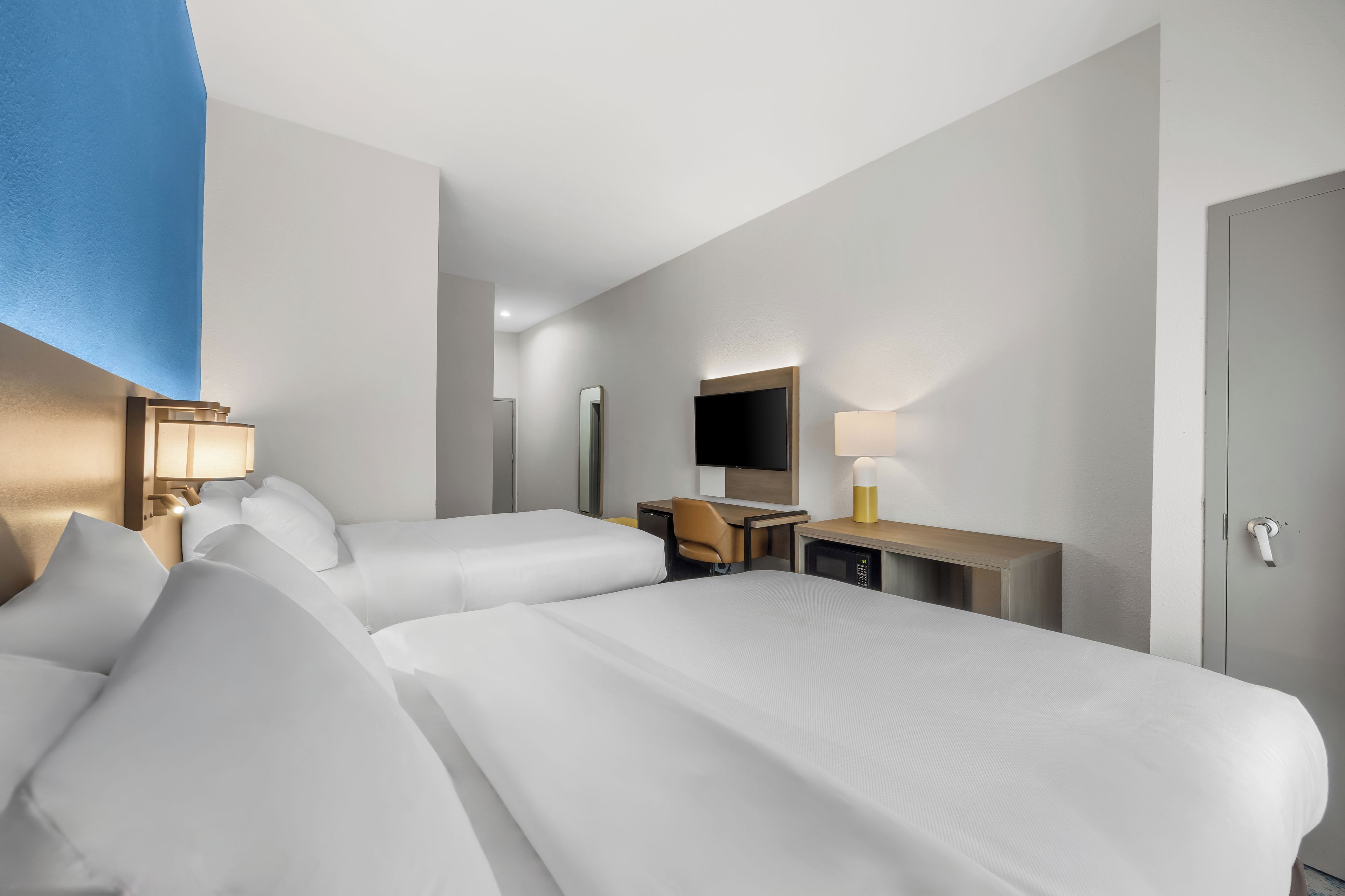 Habitación de hotel con dos camas, un escritorio, una silla, un televisor y un armario.