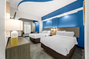 Habitación de hotel con dos camas, un escritorio con lámpara y un ventanal con cortinas.