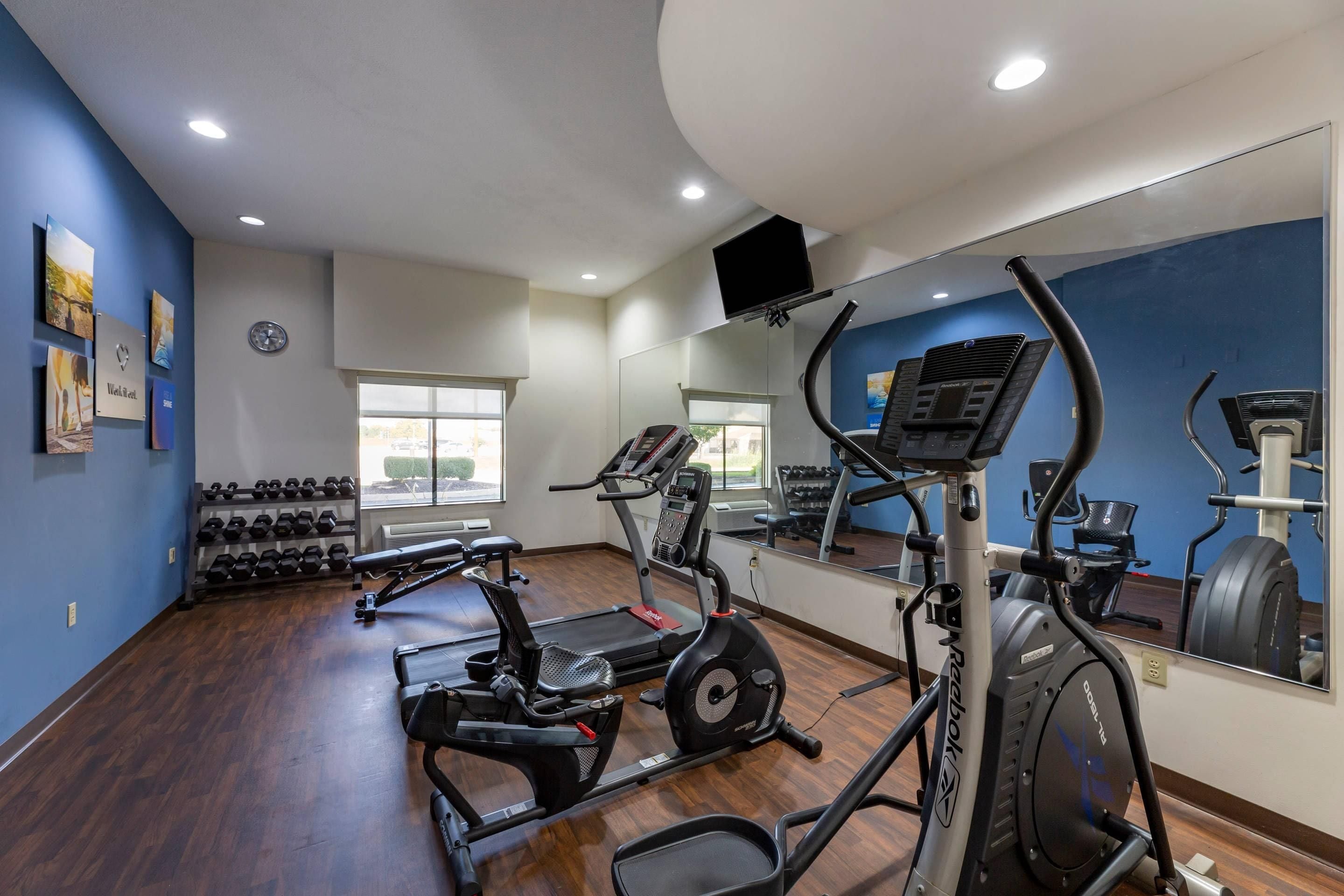 Ein Fitnessstudio mit Cardiogeräten, Hanteln und einem Spiegel.