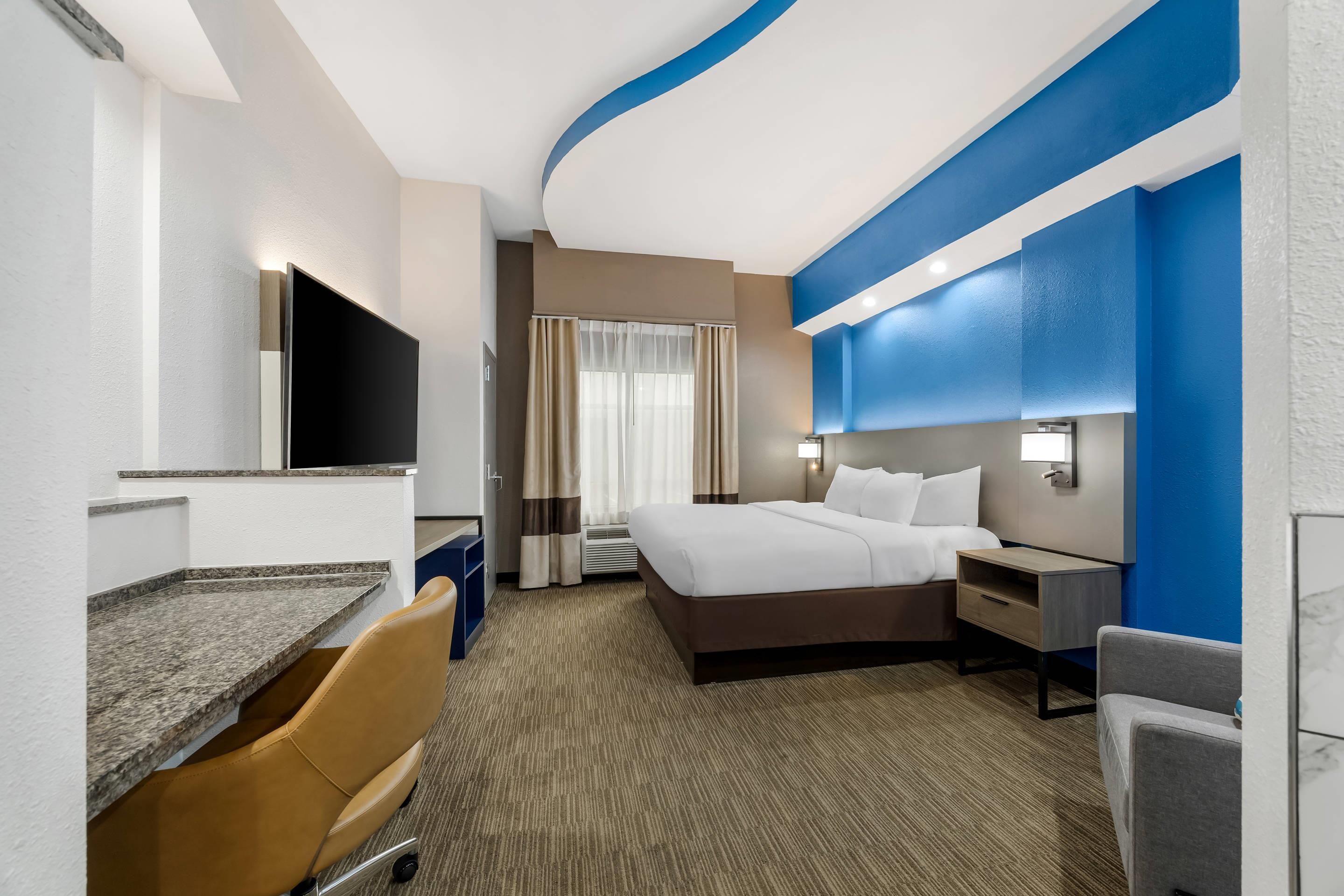 A hotel room with a bed, desk, chair, and a television.