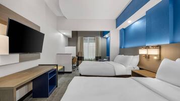 A hotel room with a large flat-screen TV, two beds, a desk, and a seating area.