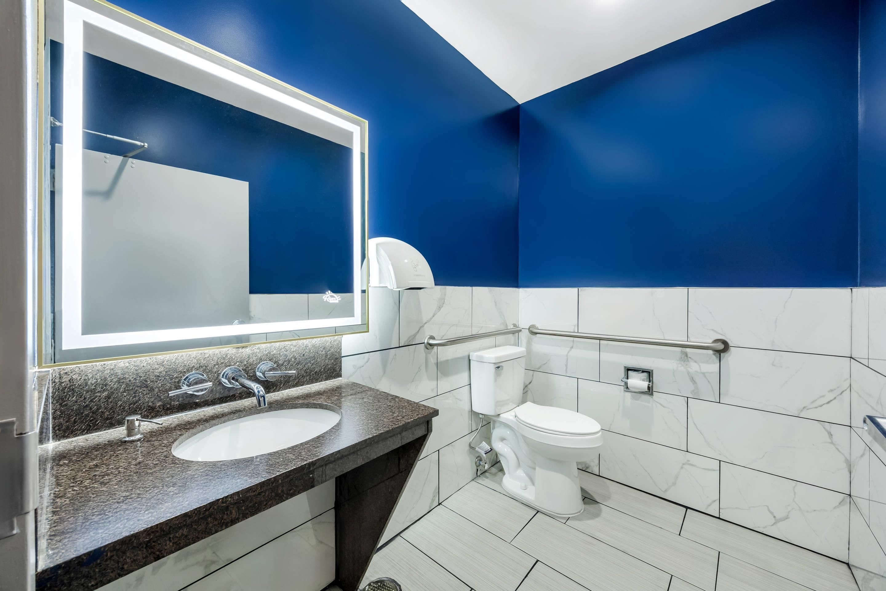 Ein modernes Badezimmer mit großem Spiegel, Waschbecken, Toilette und einem Händetrockner.