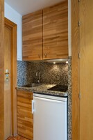 A compact kitchen with wooden cabinets, a granite countertop, a stainless steel sink, and a white refrigerator.