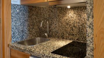 A compact kitchen with wooden cabinets, a granite countertop, and a built-in dishwasher.
