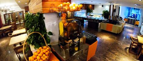 A buffet setup with a fruit display, a beverage dispenser, and seating arrangements.