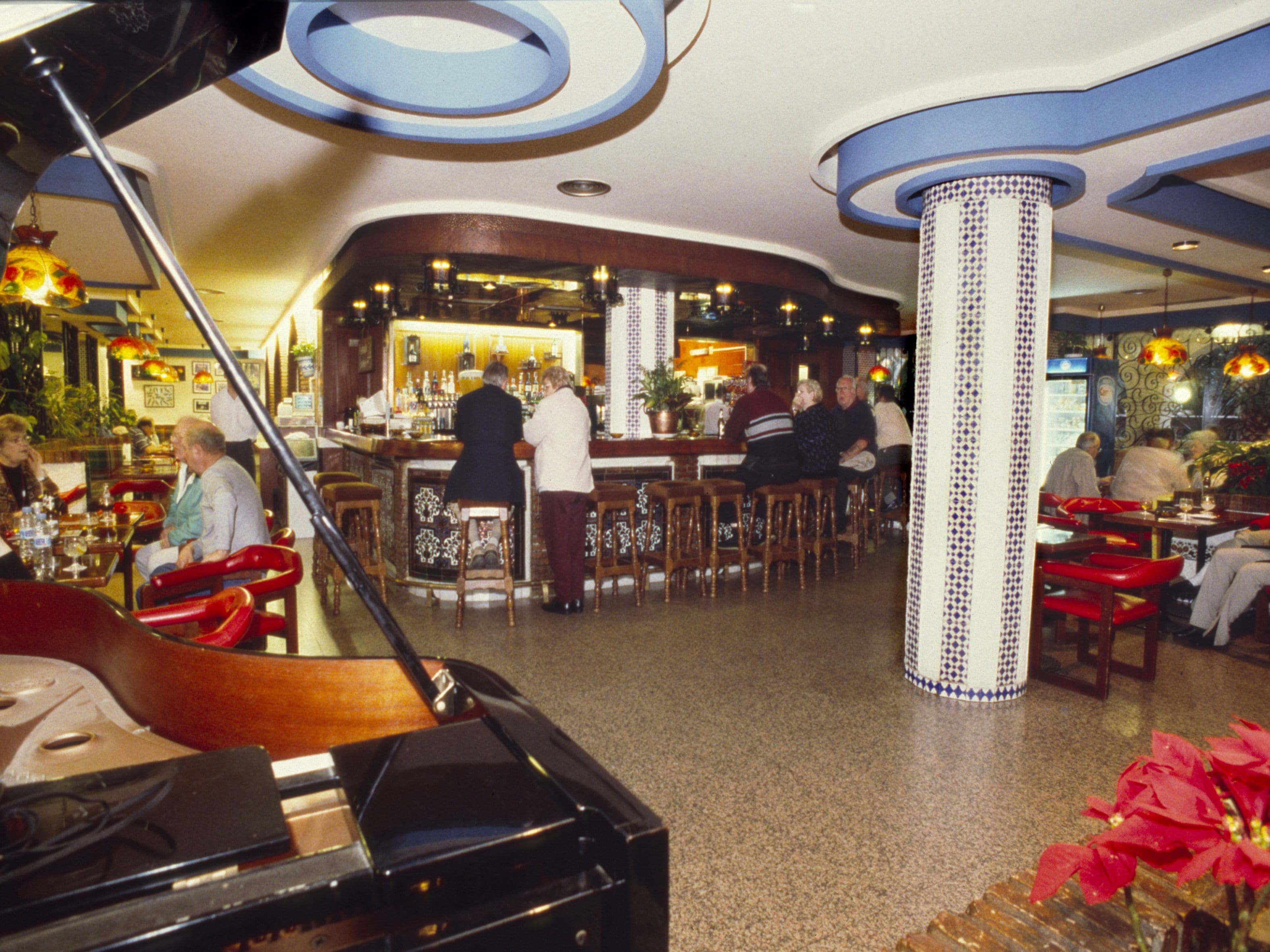 Um restaurante com área de bar, cadeiras de madeira e um piano.