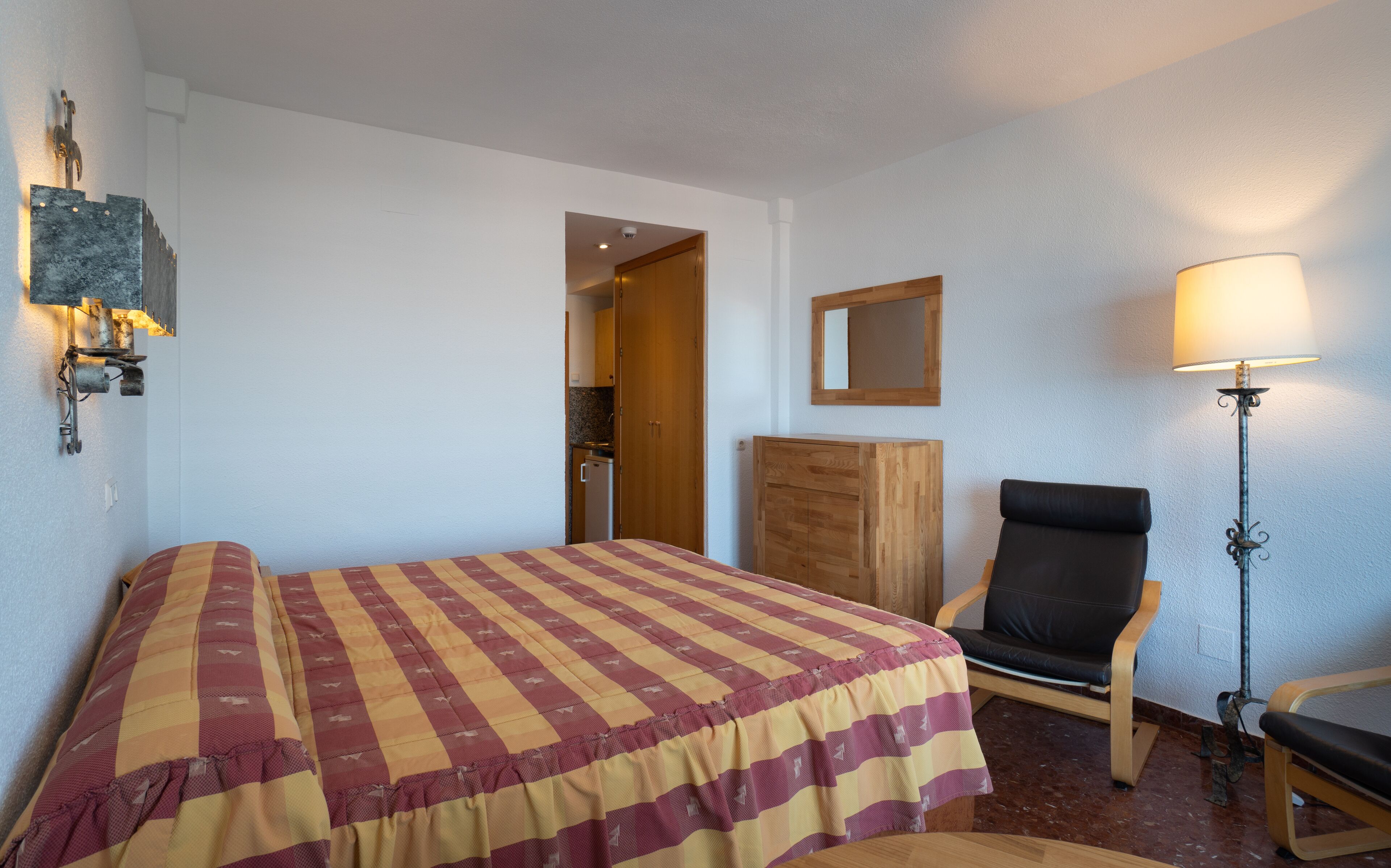 Una camera d'albergo con un letto, una poltrona, una scrivania, una lampada e un armadio.