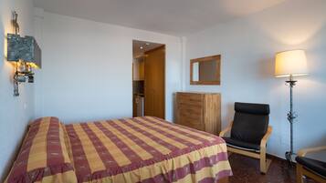 Una habitación de hotel con cama, una silla, un escritorio, una lámpara y un armario.