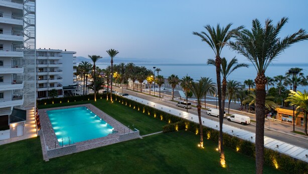 Un hotel con piscina, palmeras y vista al mar.