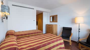 Habitación de hotel con dos camas, un armario de madera, una silla, un escritorio, una lámpara y un espejo.