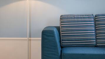 Una habitación con un sofá azul, una lámpara de pie blanca y un objeto decorativo en la pared.