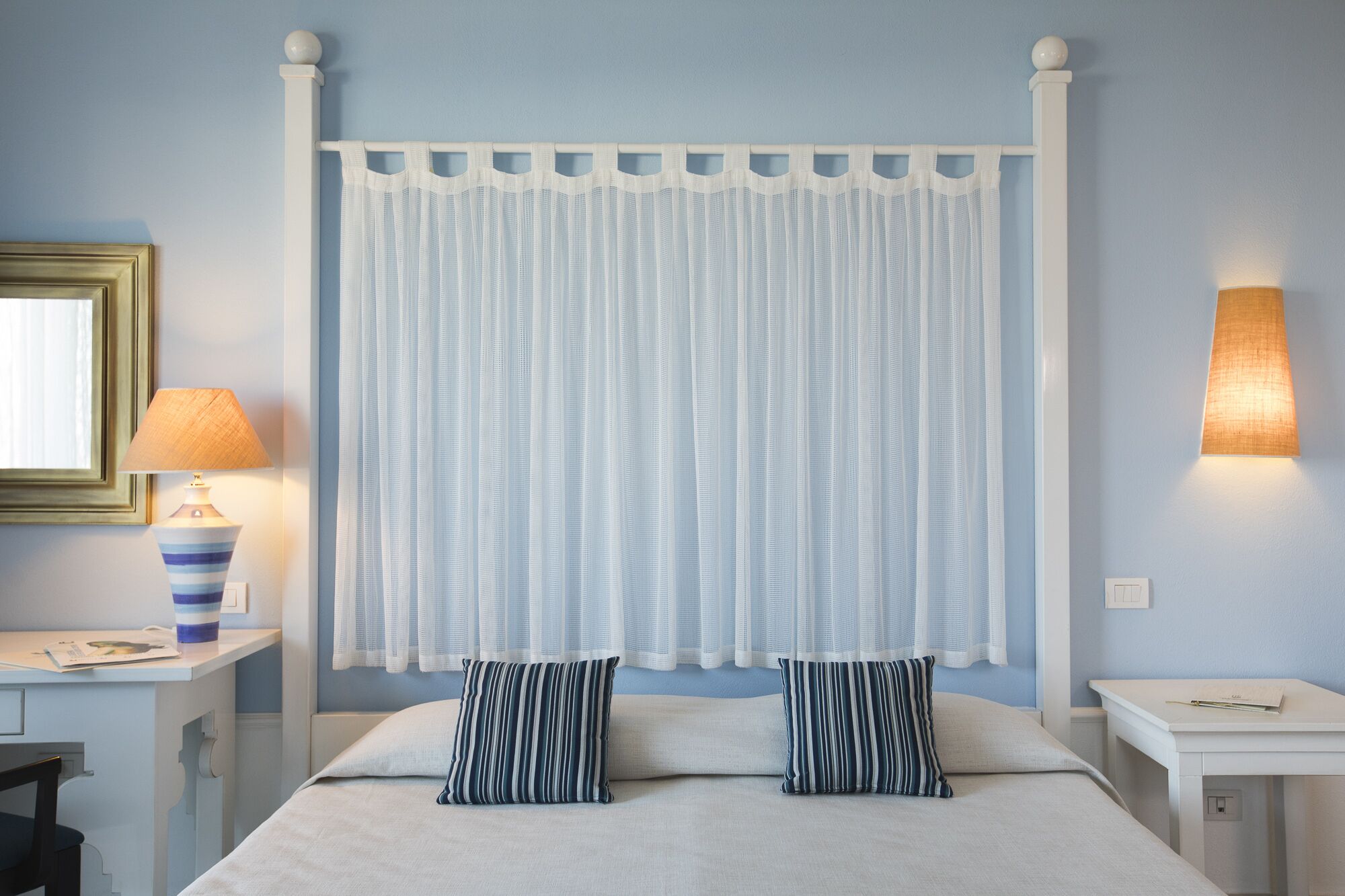 A bedroom with a bed, two pillows, a nightstand, a lamp, and a wall-mounted light fixture.