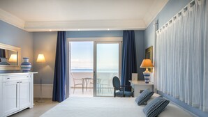 A hotel room with a bed, a desk with a lamp, a chair, and a view of the sea through a glass door.