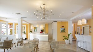 A hotel lobby with wicker furniture, a reception desk, and a large chandelier.