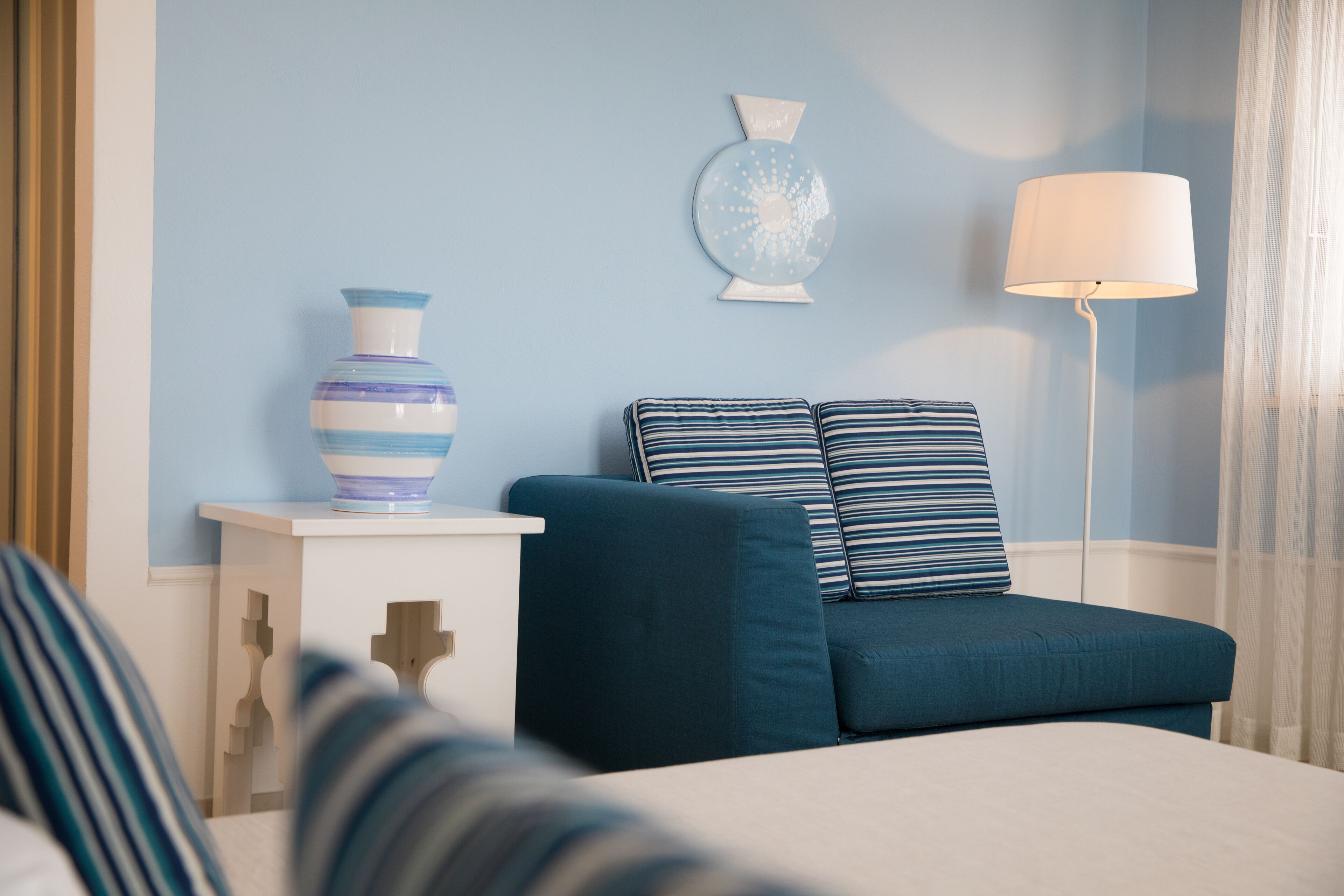 Un dormitorio con una cama, una mesita de noche con un jarrón, una lámpara y una pared decorada con un plato.